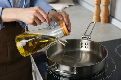 Photo of Vegetable fats. Woman pouring cooking oil into frying pan on stove in kitchen, closeup
