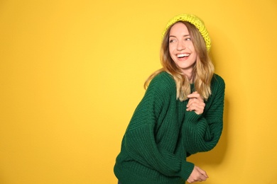 Image of Happy young woman wearing warm sweater and knitted hat on yellow background. Space for text