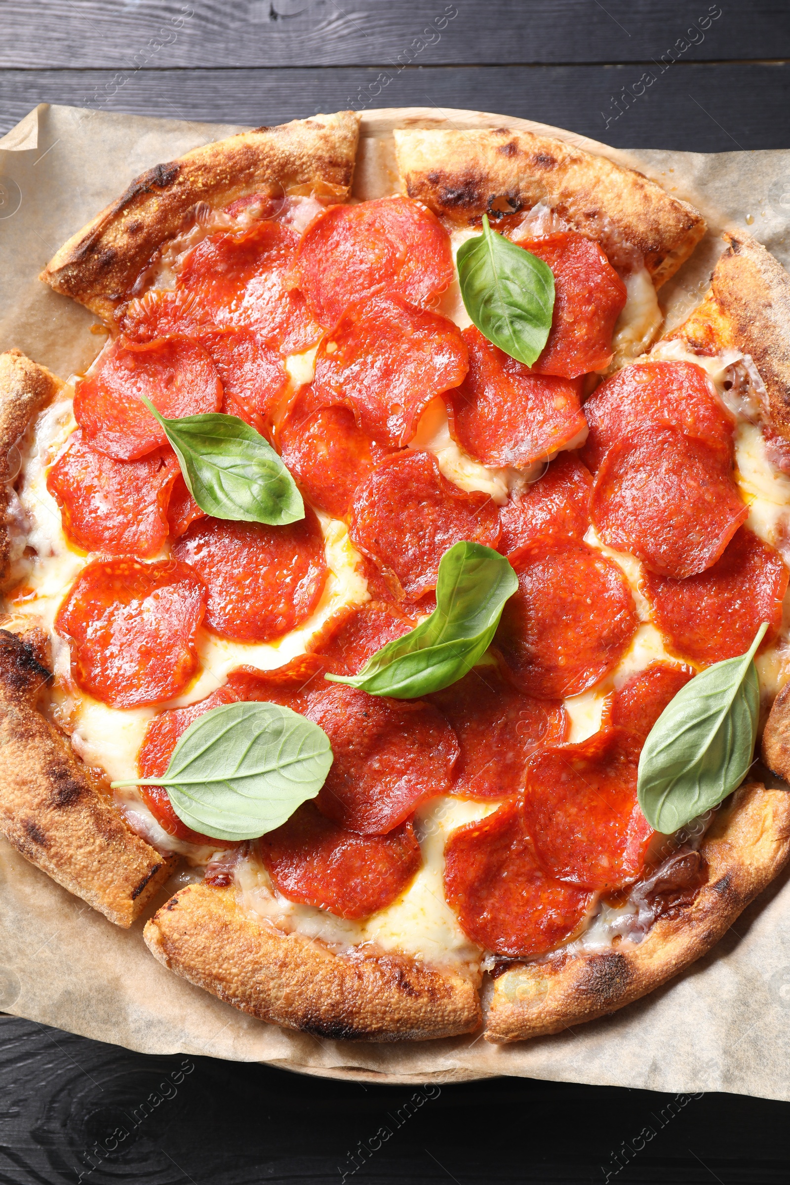 Photo of Tasty pepperoni pizza with basil on black wooden table, top view