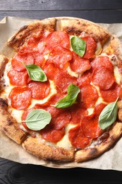 Tasty pepperoni pizza with basil on black wooden table, top view