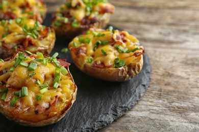 Photo of Slate plate with baked potatoes on wooden table, closeup. Space for text