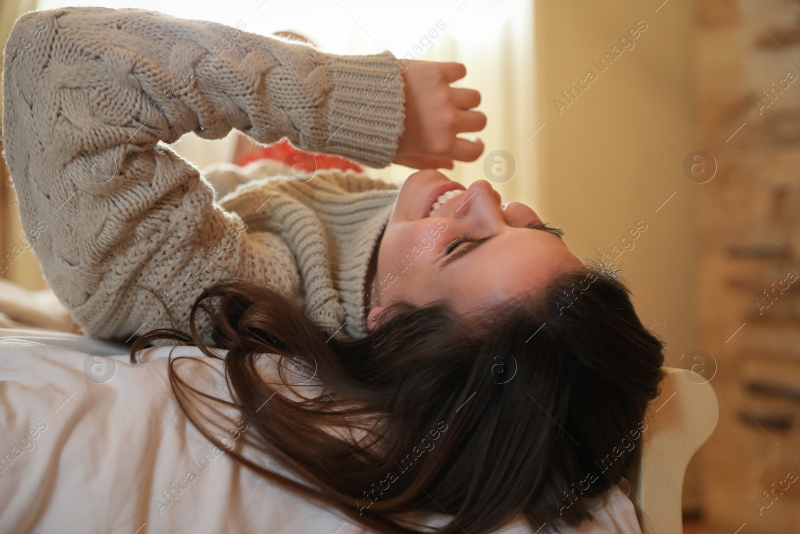 Photo of Young woman wearing warm sweater on bed at home