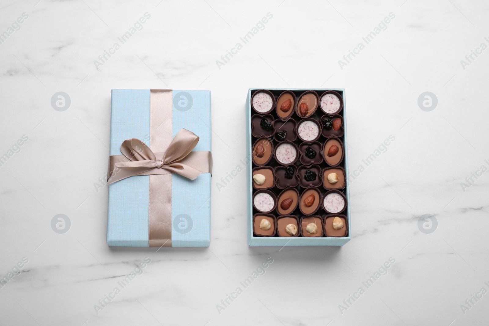 Photo of Open box of delicious chocolate candies on white marble table, top view