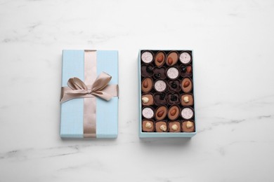 Open box of delicious chocolate candies on white marble table, top view