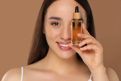 Photo of Happy young woman with bottle of essential oil on brown background