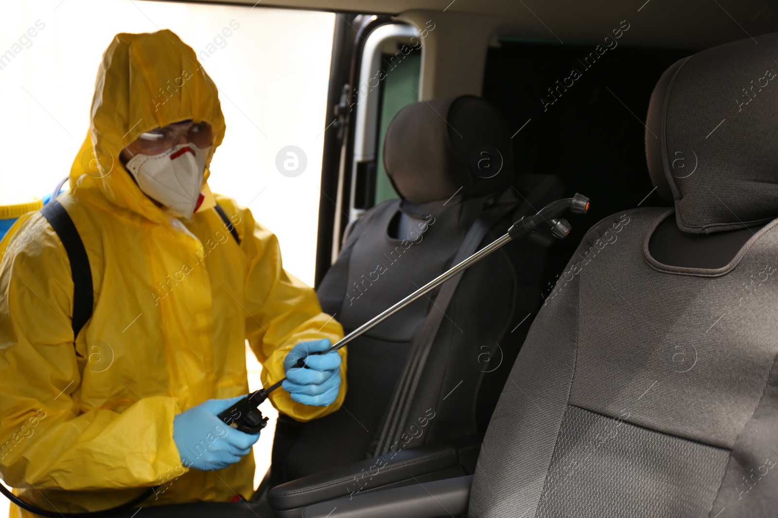 Photo of Person in protective suit disinfecting car with sprayer. Preventive measure during coronavirus pandemic