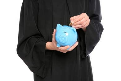 Photo of Young graduate putting coin into piggy bank on white background, closeup