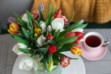 Photo of Beautiful bouquet of colorful tulips and cup with drink on grey table, closeup