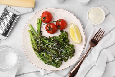 Tasty cooked broccolini with cheese, tomatoes and lemon on light table, flat lay