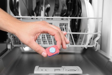 Photo of Woman putting detergent tablet into open dishwasher in kitchen, closeup