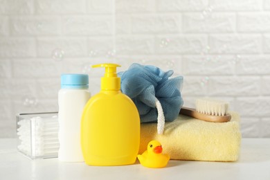 Baby cosmetic products, bath duck, brush and towel on white table against brick wall