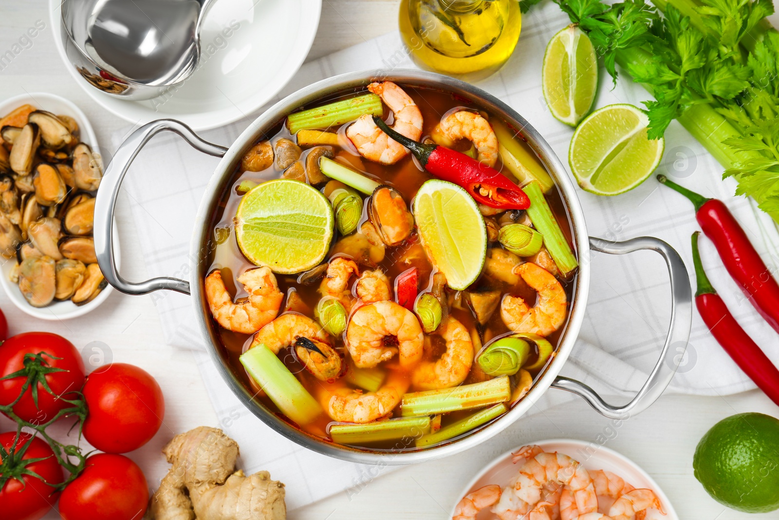 Photo of Saucepan with delicious Tom Yum soup and ingredients on white wooden table, flat lay