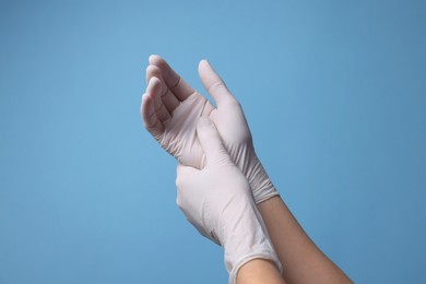 Photo of Doctor wearing white medical gloves on light blue background, closeup