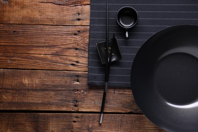 Empty iron wok, sauce bowl and chopsticks on wooden table, flat lay. Space for text