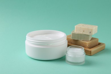 Moisturizing cream in open jars and soap bars on turquoise background. Body care products