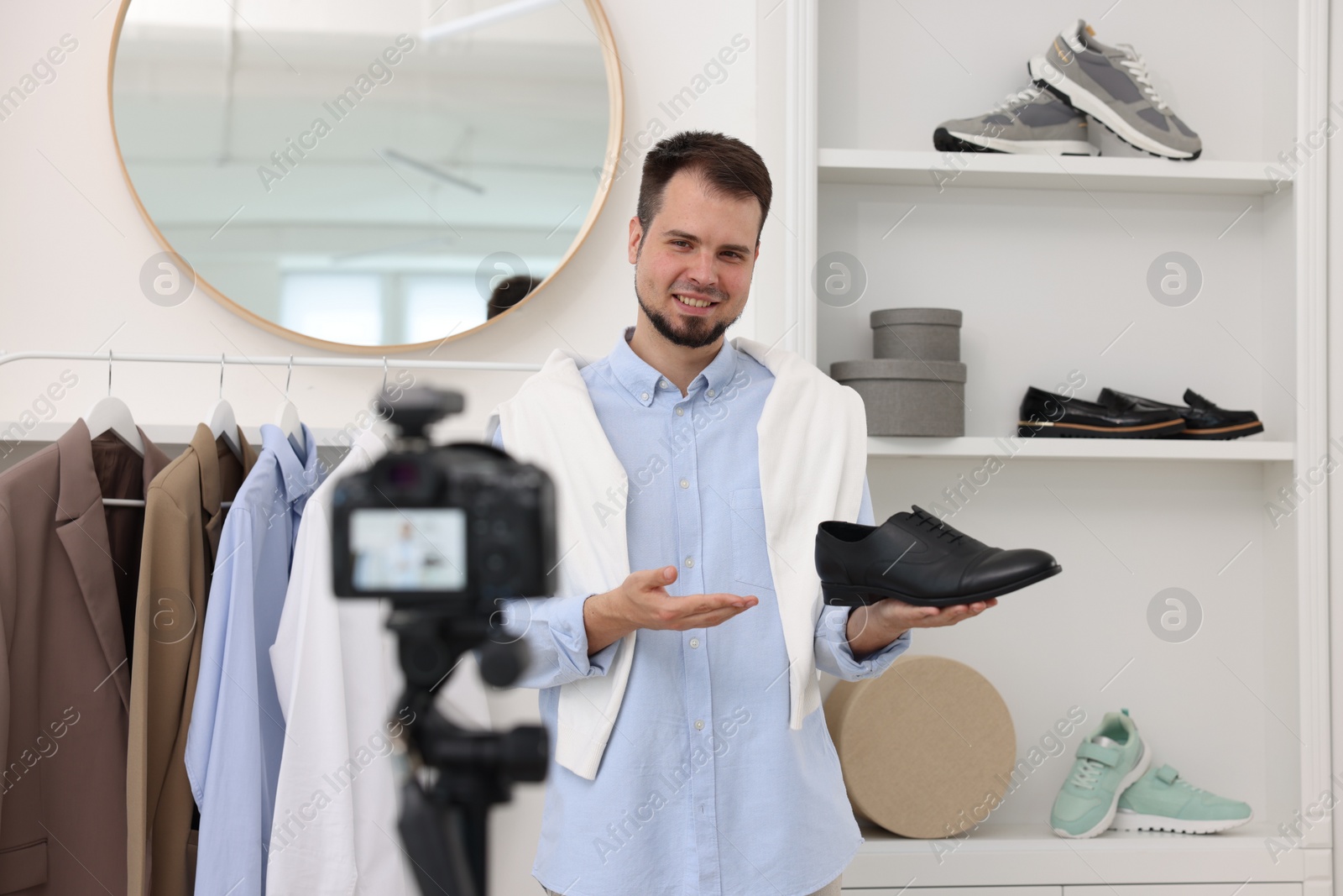 Photo of Smiling fashion blogger showing shoe while recording video at home