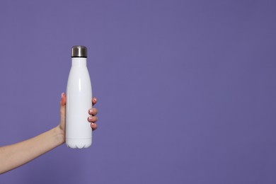 Woman holding thermos bottle on purple background, closeup. Space for text