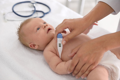 Photo of Doctor measuring temperature of little baby with digital thermometer indoors, closeup. Health care