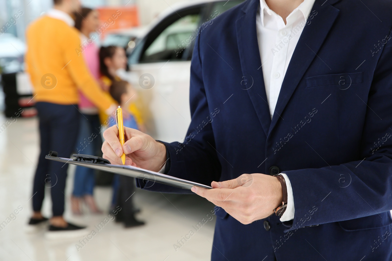 Photo of Car salesman with clipboard and blurred family on background