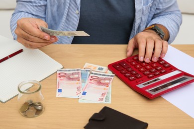 Photo of Man counting money with calculator at table indoors, closeup