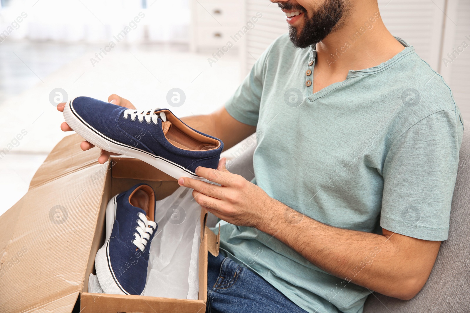 Photo of Young man opening parcel with shoes at home, closeup