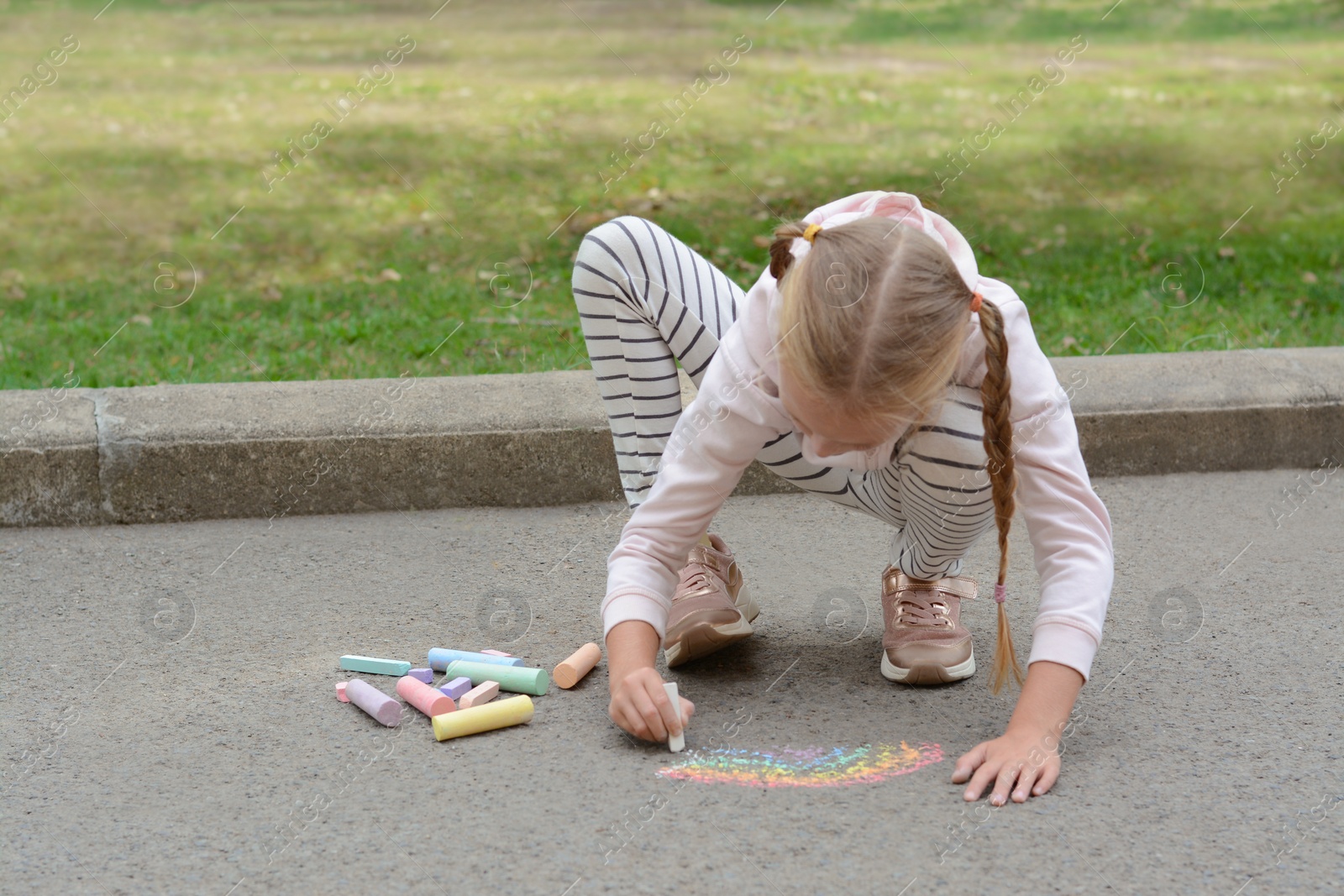 Photo of Little child drawing rainbow with chalk on asphalt