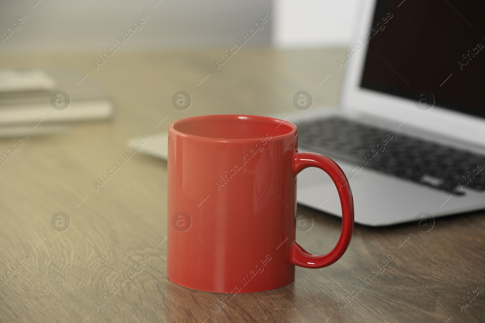 Photo of Red ceramic mug on wooden table at workplace. Mockup for design