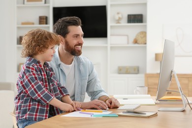 Photo of Man working remotely at home. Father and his son at desk with computer
