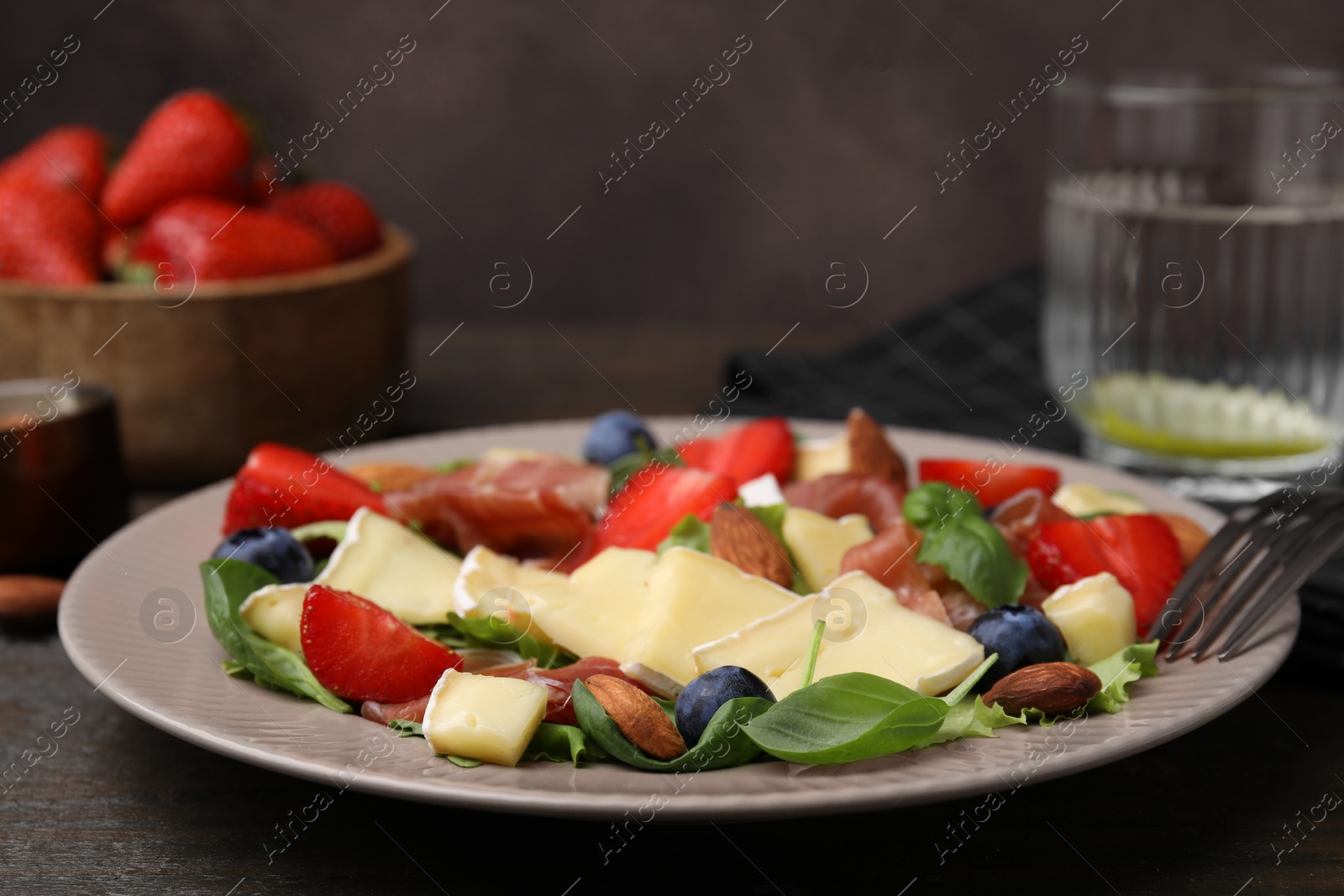 Photo of Tasty salad with brie cheese, prosciutto, almonds and berries on table, closeup