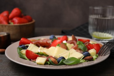 Tasty salad with brie cheese, prosciutto, almonds and berries on table, closeup