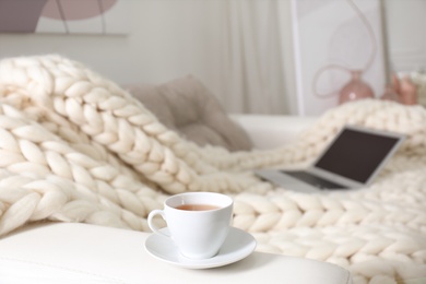 Photo of Cup of drink on couch with soft knitted blanket in living room. Interior element