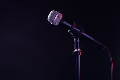 Photo of Modern microphone on stand against black background. Space for text