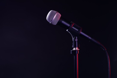 Modern microphone on stand against black background. Space for text