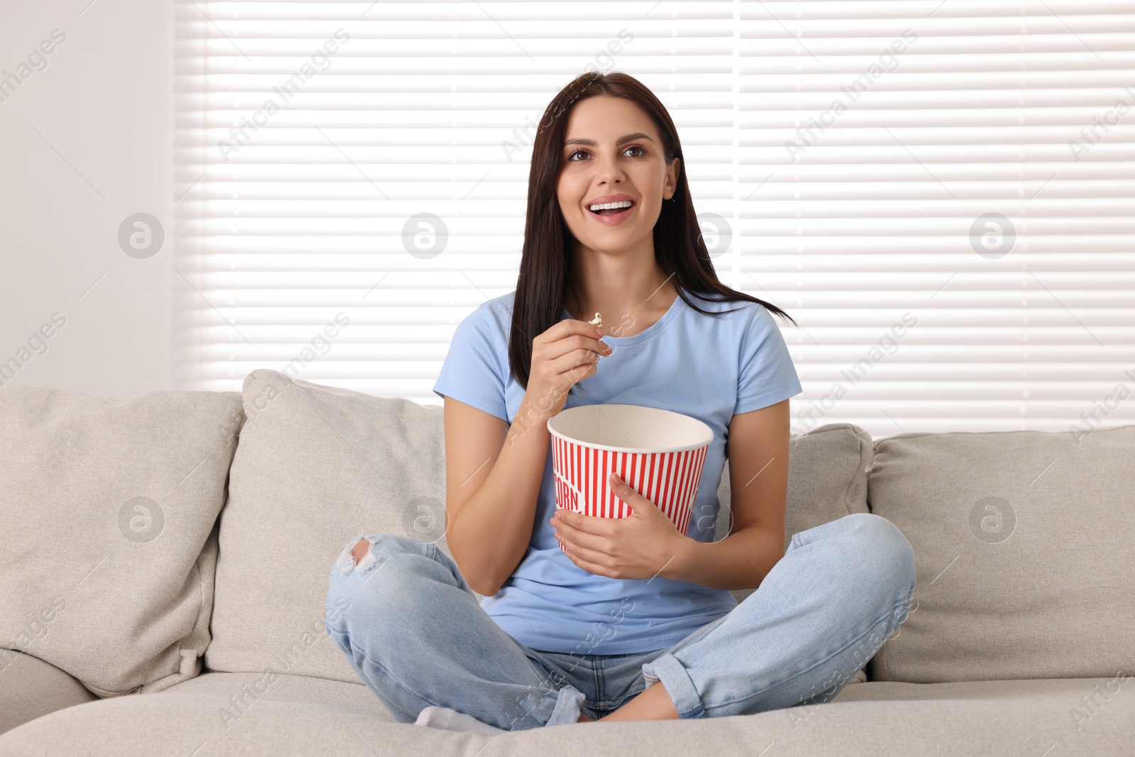 Photo of Happy woman with popcorn bucket watching TV on sofa at home