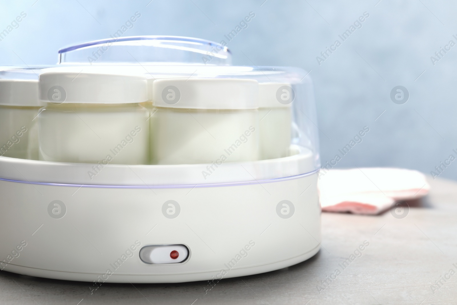 Photo of Modern yogurt maker with full jars on grey table, closeup