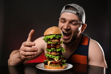 Young hungry man eating huge burger on black background