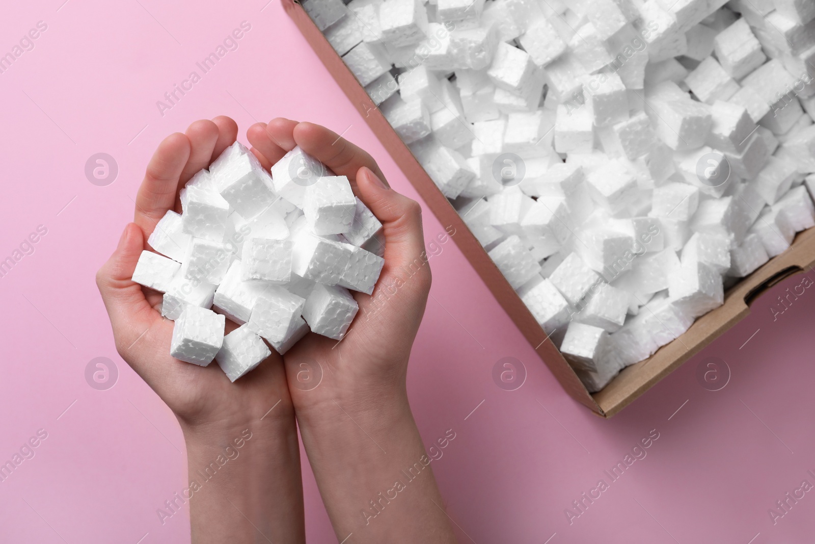 Photo of Woman with handful of styrofoam cubes on pink background, top view