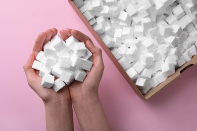 Woman with handful of styrofoam cubes on pink background, top view