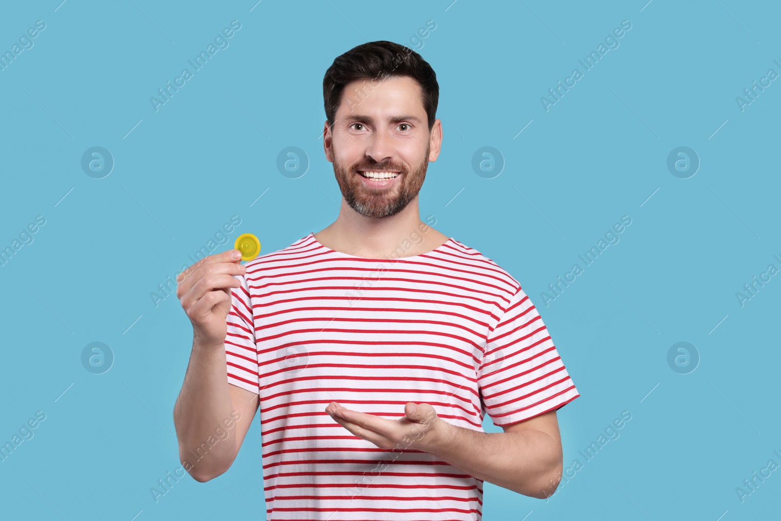 Photo of Happy man holding condom on light blue background. Safe sex