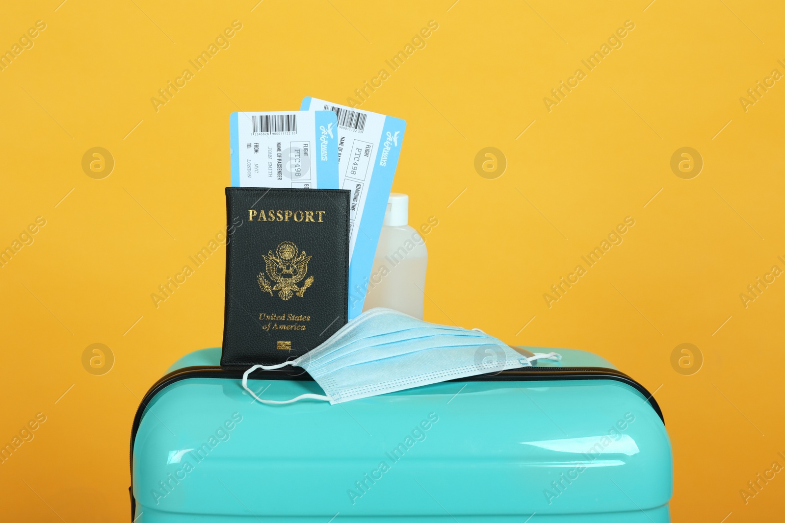 Photo of Passport with tickets, sanitizer and protective mask on suitcase against yellow background. Travel during quarantine