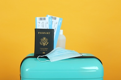 Passport with tickets, sanitizer and protective mask on suitcase against yellow background. Travel during quarantine