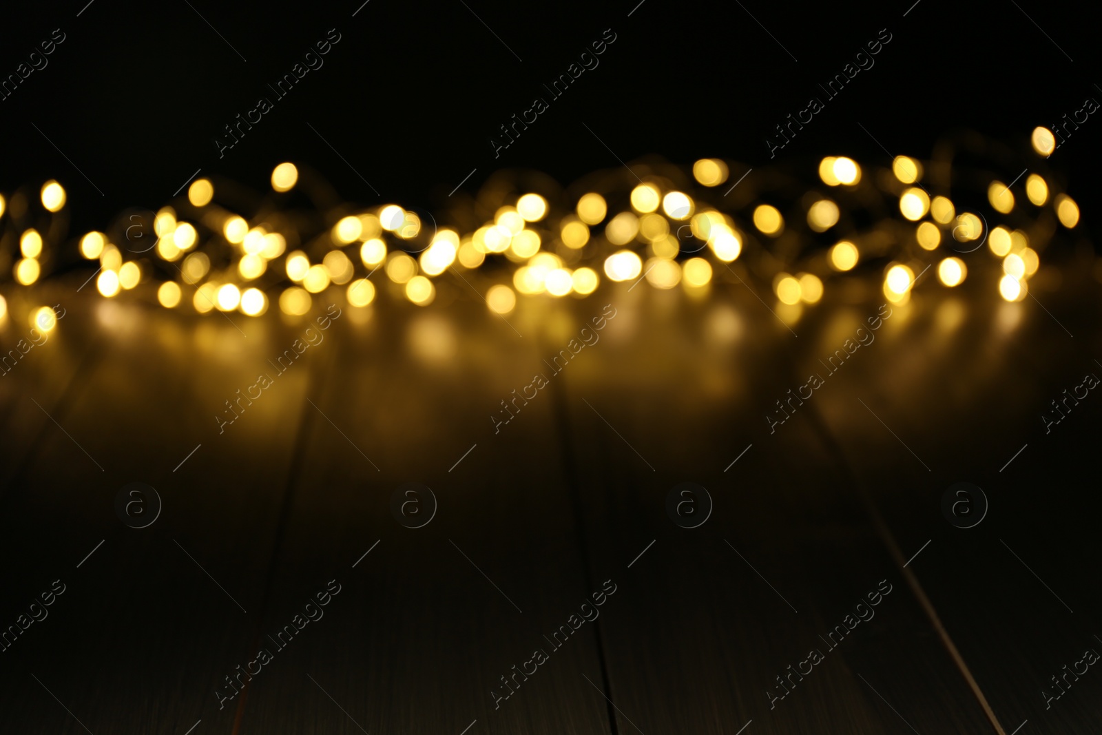 Photo of Blurred view of gold lights on wooden table, space for text