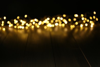 Blurred view of gold lights on wooden table, space for text