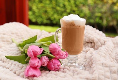 Glass of delicious cocoa and pink tulips on light blanket at terrace