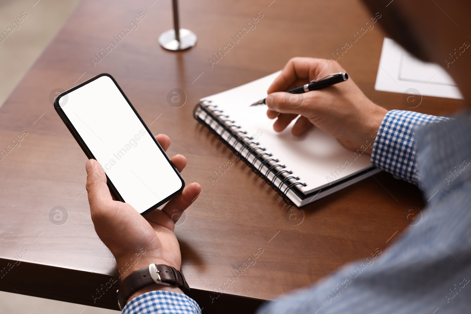 Photo of Man with smartphone writing something in notebook at table, closeup