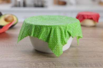 Photo of Bowl covered with beeswax food wrap on wooden table in kitchen