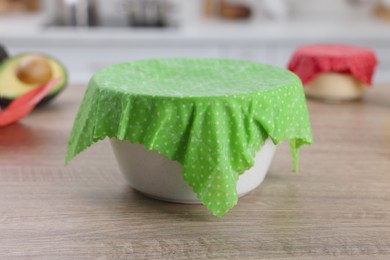 Bowl covered with beeswax food wrap on wooden table in kitchen