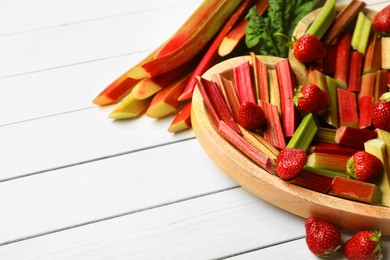 Photo of Cut fresh rhubarb stalks and strawberries on white wooden table, space for text