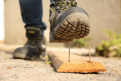 Careless worker stepping on nail in wooden plank outdoors, closeup