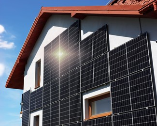 Photo of House with installed solar panels on wall under blue sky. Alternative energy source